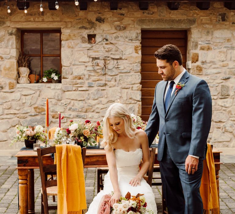 Bride and groom sat at their outdoor wedding table, the grooms hand on the bride's shoulder