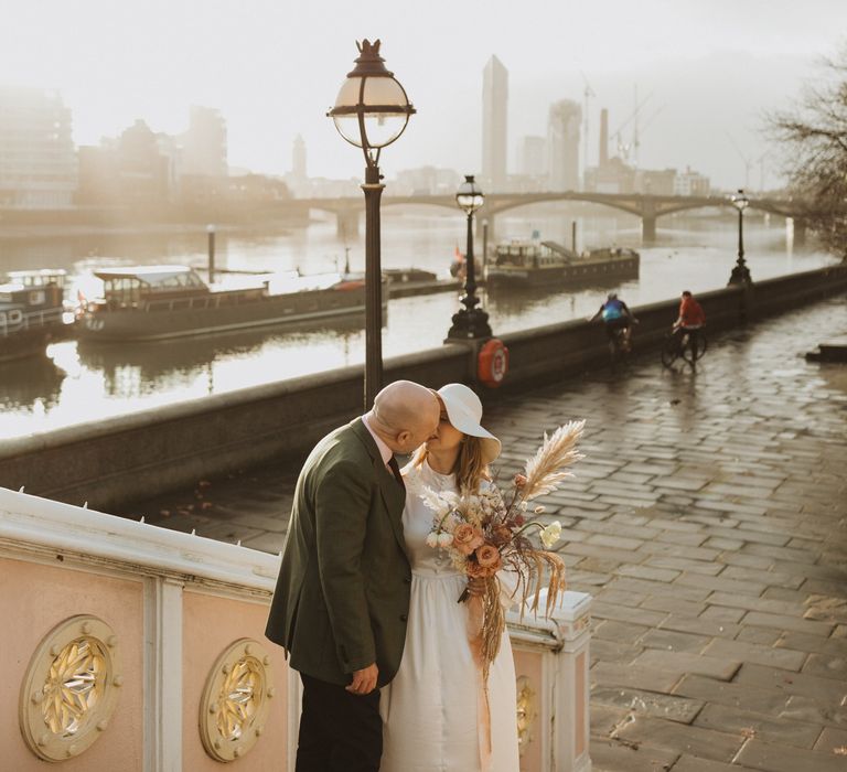 Bride & groom kiss on the bride with river in the background