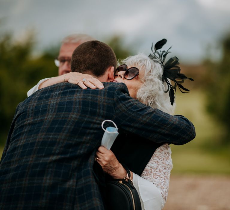 Groom in a navy and brown check wool suit embracing his wedding guest 