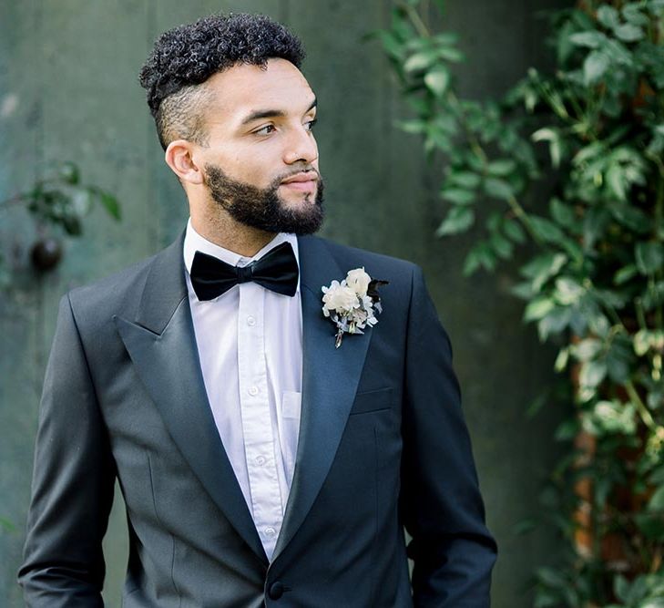 Bearded groom in a tuxedo and bow tie with white buttonhole flower 