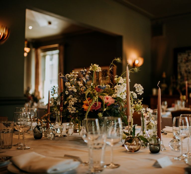 Interior of Hotel du Vin Harrogate set for wedding breakfast with long brown candles, white and pink floral centrepieces and glassware