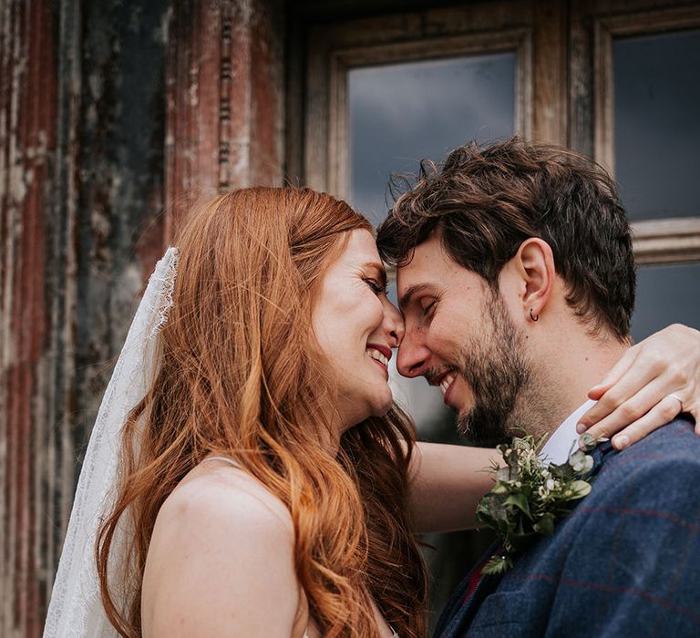 Intimate bride and groom portrait with bride with long wavy red hair wearing a delicate lace cathedral length veil