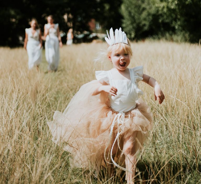 Flower girl in a blush tutu and feather headdress running through the fields | Rosie Kelly Photography