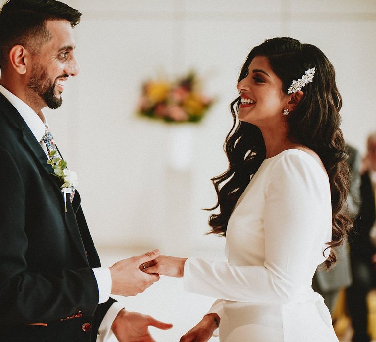 Bride in a long sleeve Chi Chi London wedding dress with side swept wavy hair and diamanté clip holding hands with her husband at their Brent Civic Centre Wedding 