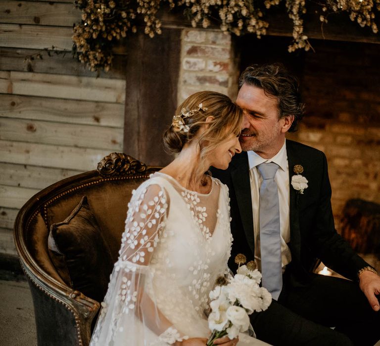 Bride and groom sat together on vintage sofa for rustic luxe wedding ceremony