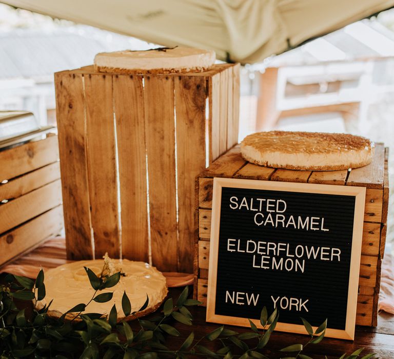 Three cheesecakes on wooden boxes with black sign inside tipi at garden wedding reception