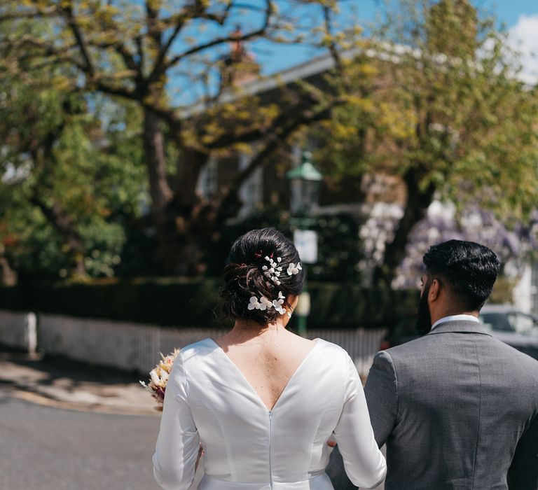 Bride & groom walk away from camera as bride wears her dark hair pulled back complete with soft petal inspired hair accessories 