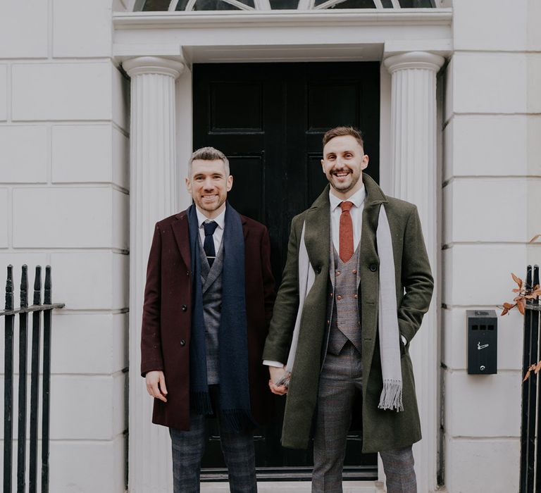 Grooms stand in front of black door and white building on their wedding day within London