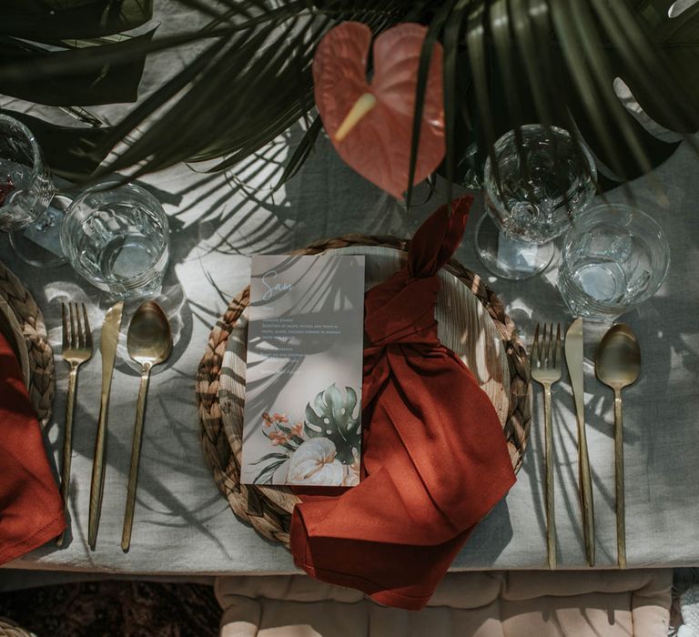 Tropical boho wedding table set outside with tropical florals, red napkins and gold cutlery on low white table for birds of paradise wedding inspiration