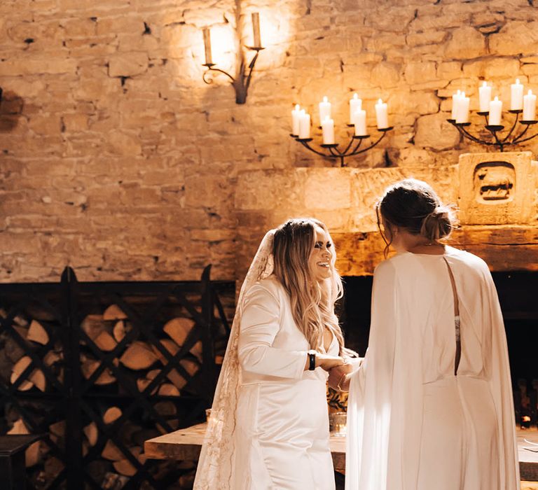 Brides look lovingly at one another as they hold hands and smile during ceremony