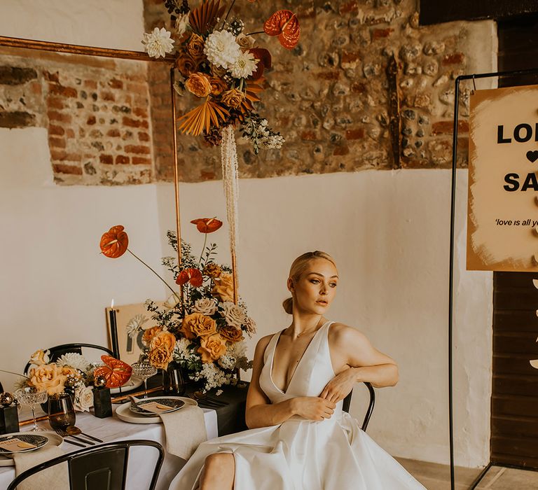 Beautiful bride with sleek back bridal bun sitting at her intimate tablescape in a Jesus Peiro wedding dress with front split design 