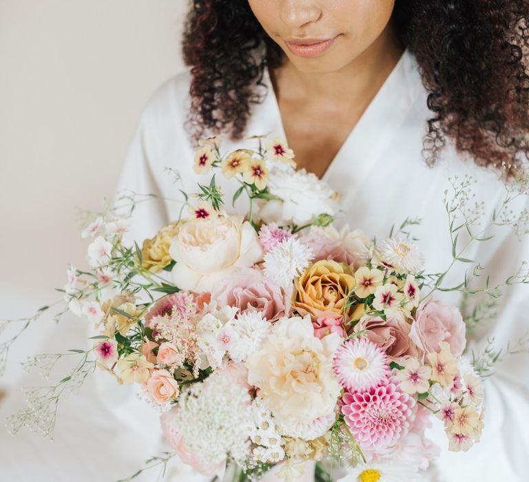 Black bride with naturally curly hair holding a light pink and white wedding bouquet with subtle natural wedding makeup 