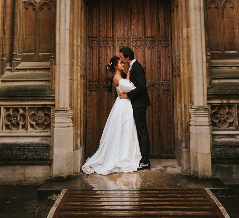 Groom in a tuxedo kissing his brides forehead at the historic doors of Bodleian Library 