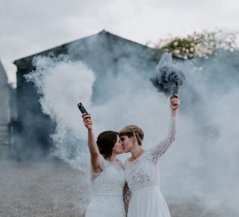 Portrait of two brides kissing and holding green and white flares in the air 