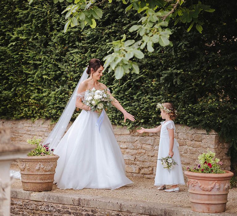 Bride holds out her hand to flower girl as they walk down the aisle on her wedding day