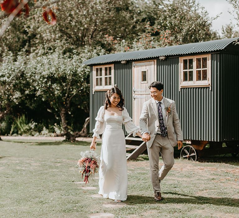 Bride & groom walk across gardens on their wedding day