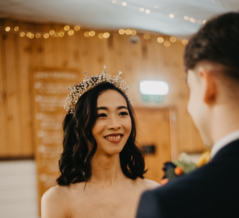 Smiling bride in strapless feathered wedding dress and bridal headband smiles at groom during rustic wedding ceremony at The Wellbeing Farm in Lancashire