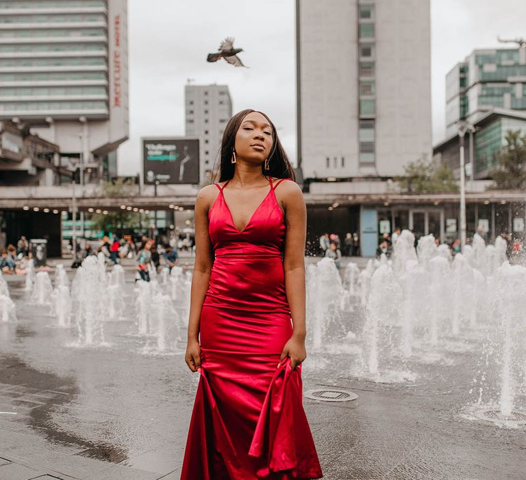 Bride wears bright red satin gown in front of fountains