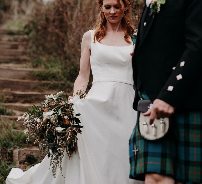 Bride in an April Ross wedding dress holding a foliage and anemone wedding bouquet by her side 