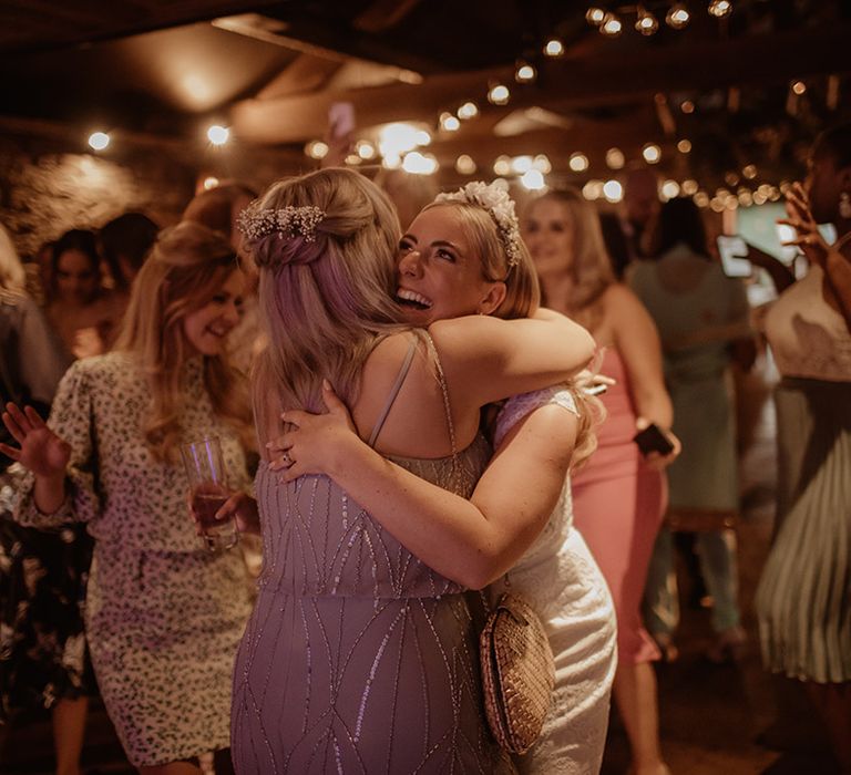 Bride in an appliqué headdress embracing a wedding guest on the dance floor 