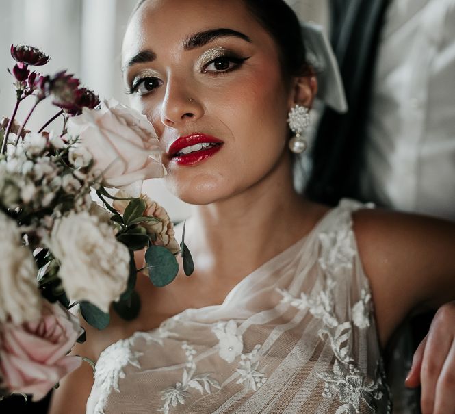 Bride wears deep red lipstick whilst holding floral bouquet