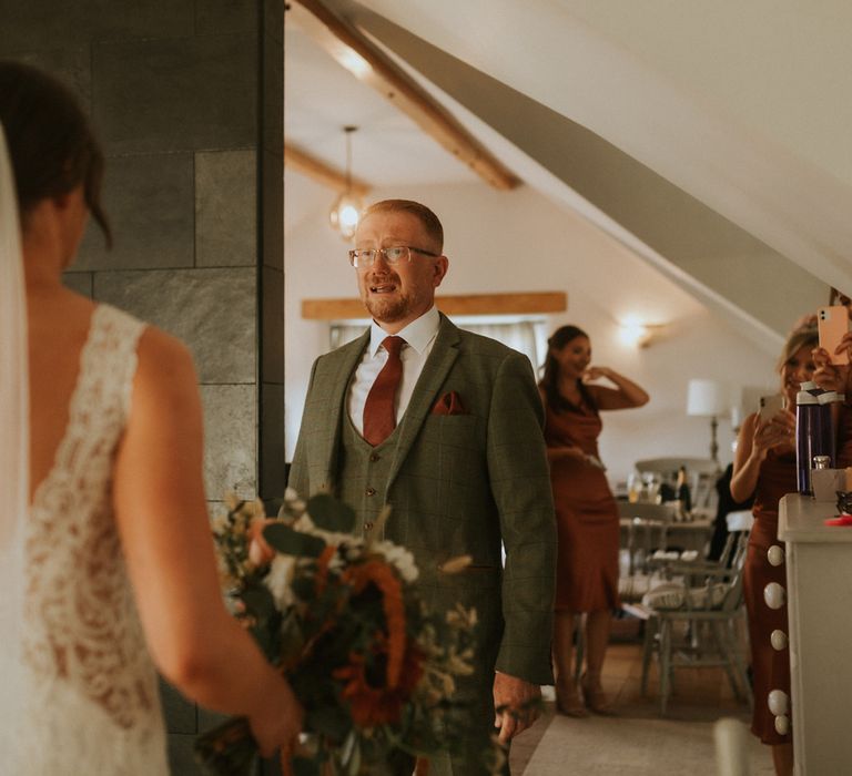 Emotional wedding guests in green three piece suit and burgundy tie and pocket square gets fist look at bride in lace wedding dress and veil