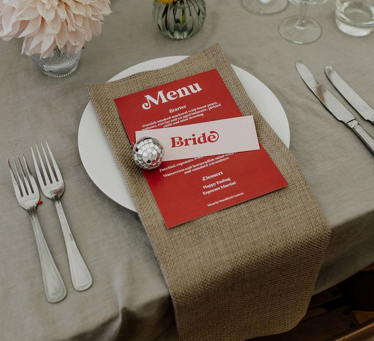 Place setting with burlap napkin, menu card, mini disco ball and flower stems in bud vases 