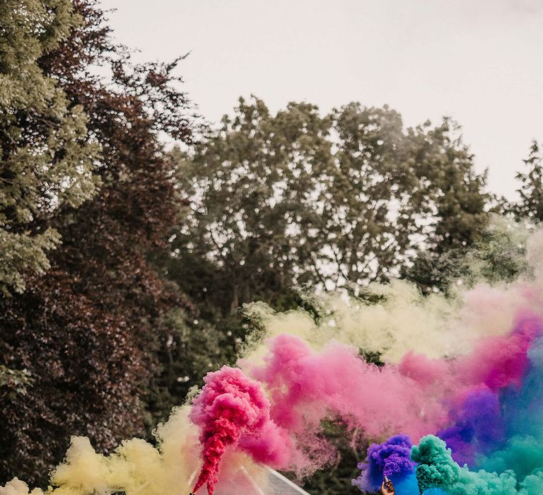 Bride & groom stand with their wedding party and let off colourful smoke bombs