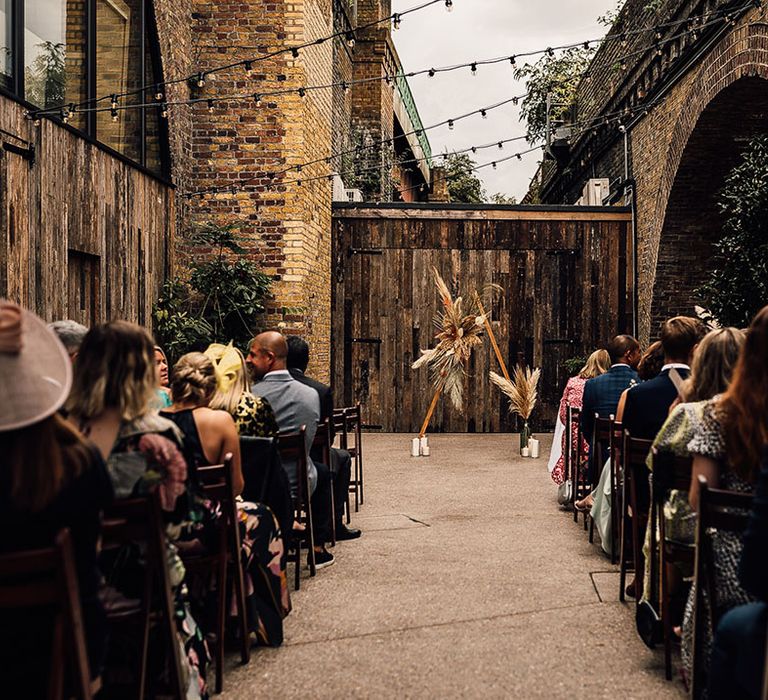 wedding ceremony in the courtyard at 100 Barrington with wooden triangle altar decorated in dried and fresh flowers 