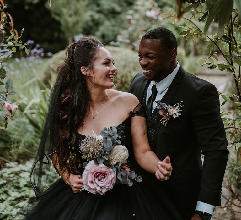 Bride looks lovingly at her groom as she holds pastel bouquet complete with green foliage