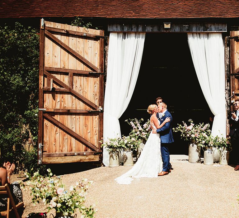 Bride in boho lace wedding dress kisses groom in blue suit 