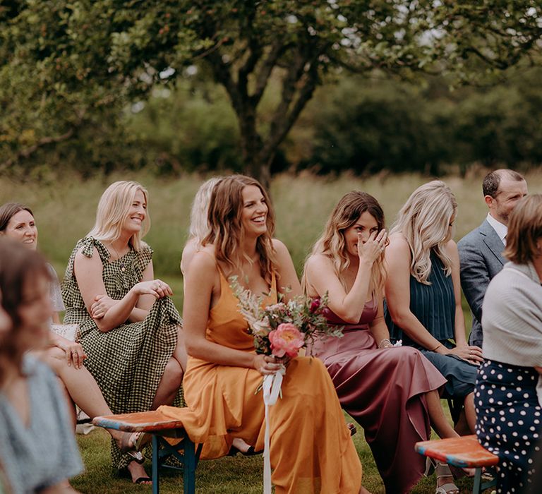 wedding guests laugh and wipe tears as they watch the wedding ceremony take place