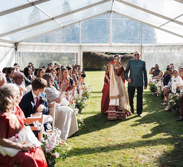 Bride is walked down the aisle wearing traditional attire for Indian wedding ceremony 