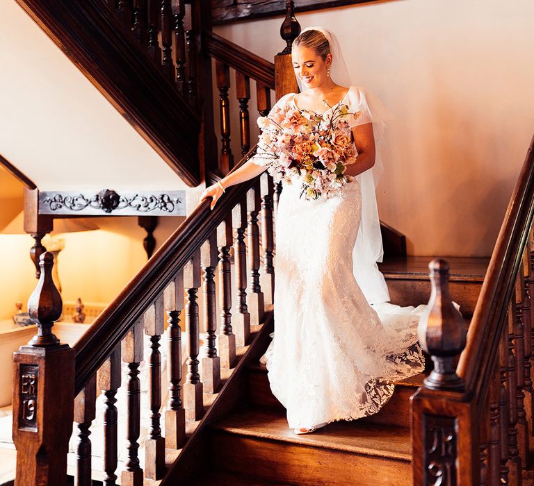 Bride with sleek blonde updo and veil descends the stairs in ruffle sleeve lace wedding dress from Emmy Mae