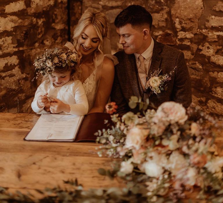 Bride and groom sign their wedding register with their daughter wearing a flower crown 