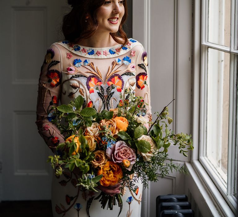 Bride in white wedding dress with bright and colourful flower detail with blue, orange and yellow bouquet