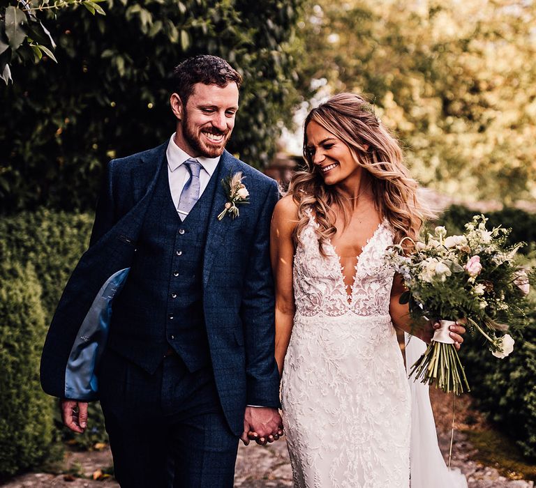 Groom in blue three piece suit and bride in lace v-neck wedding dress walk together