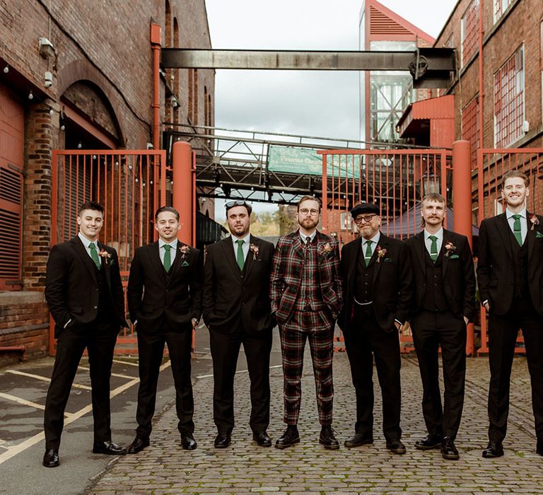 Groom wears bespoke tartan suit and stands with his groomsmen who wear three piece suits complete with green ties and pocket squares 