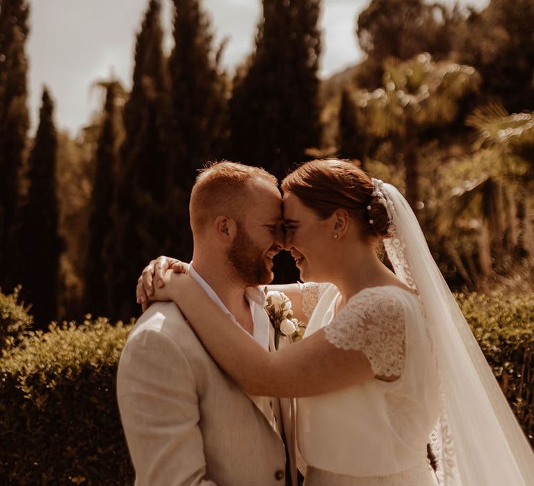 Bride & groom stand outdoors in Spain on their wedding day in front of tropical trees and rolling hills backdrop 