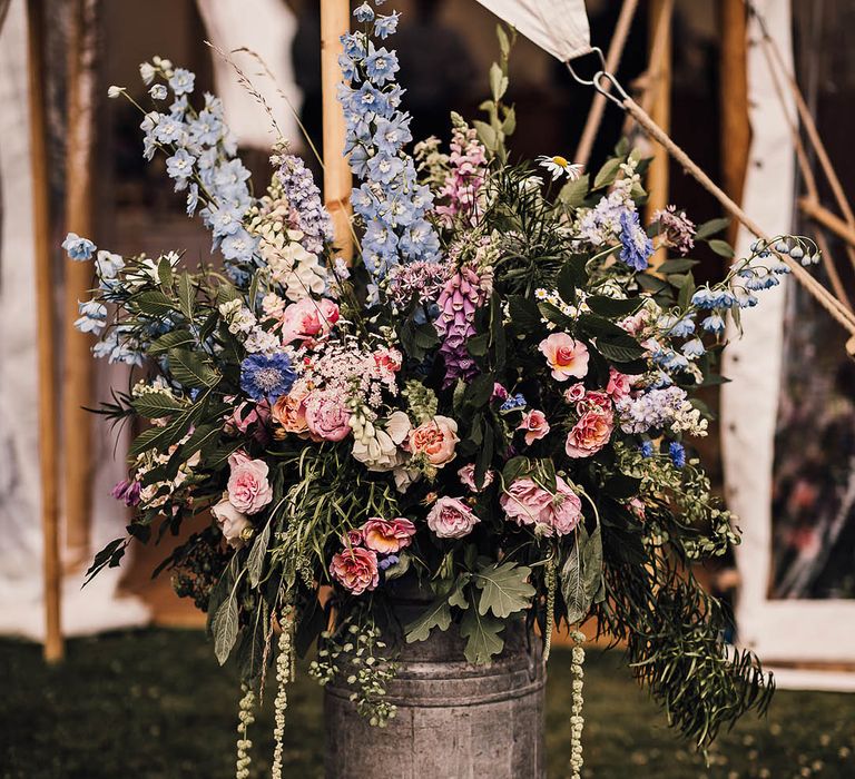 A vintage milk churn full of pink and blue wildflowers for the traditional marquee wedding 