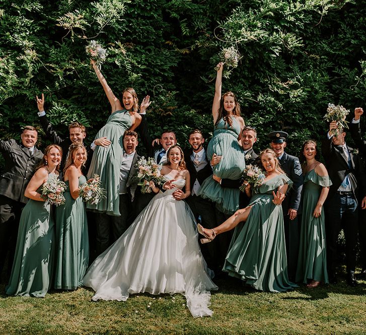 Bride & groom stand with their groomsmen and bridesmaids in green dresses for fun wedding picture