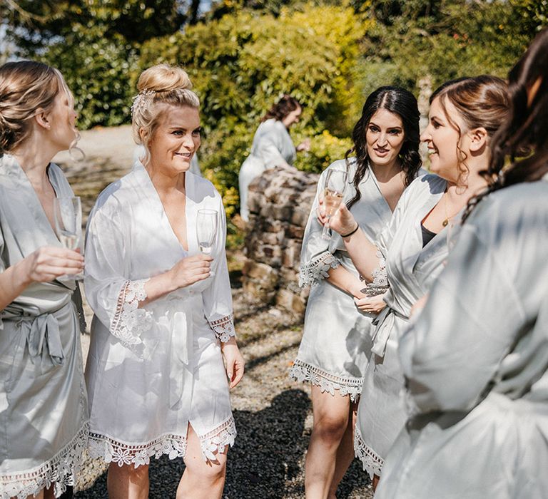 Bride in white satin robe with bridesmaids in pale green dresses with a floral pattern