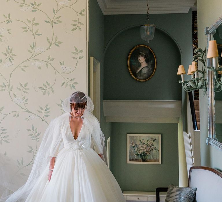 Bride wears hood styled cathedral veil and tulle princess skirt wedding dress with floral embellishment to waist 