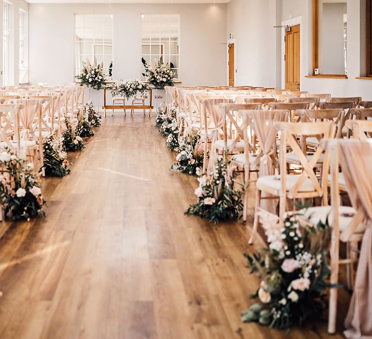 Aisle complete with wooden chairs lined with neutral toned floral arrangements and floral arch