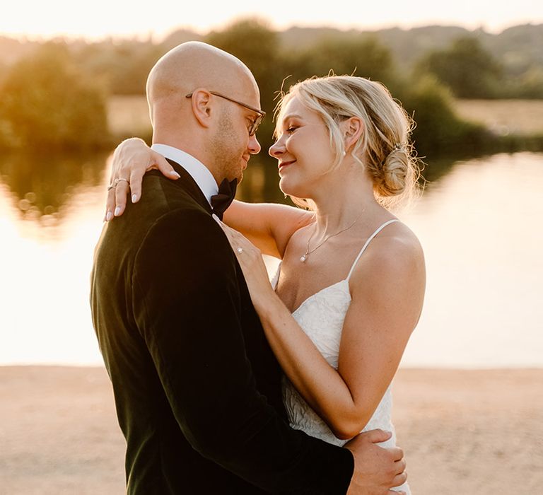 Bride wearing lace fitted wedding dress embraces her groom during golden hour at Bisham Abbey