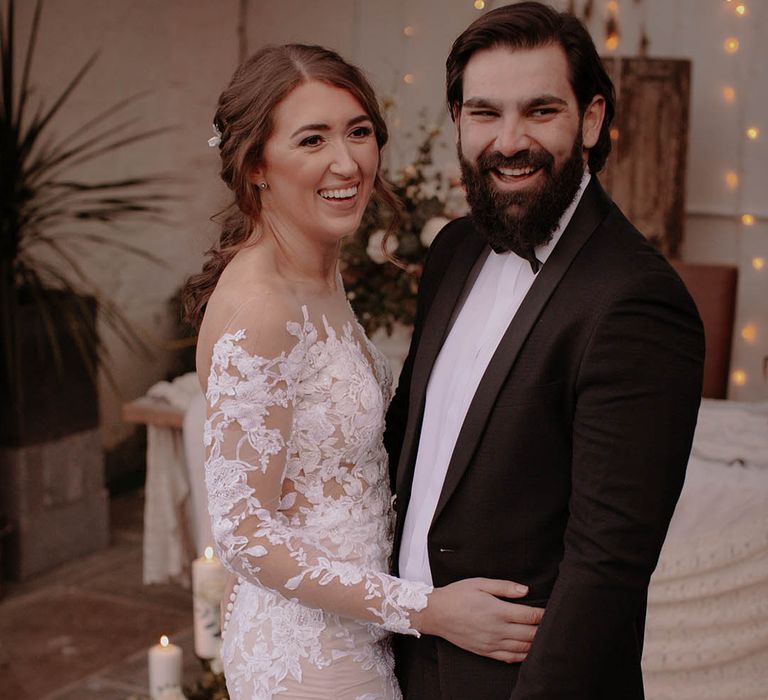 Bride in an illusion lace wedding dress with long sleeves and the groom in black tie for the rustic winter wedding 