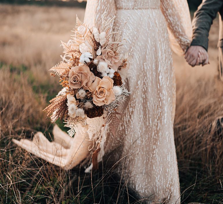 Bride holds dried floral bouquet tied with burnt orange ribbon