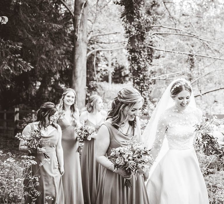 Bridesmaids in taupe dresses walk with the bride in a high neck long sleeve lace Suzanne Neville wedding dress 