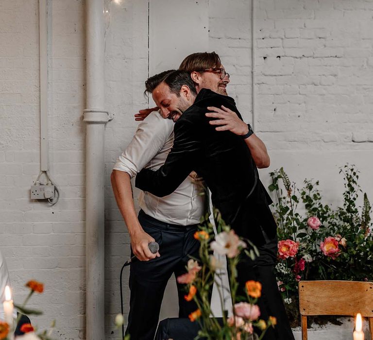 Groom in dark tux hugging wedding guest at Stylish Hackney Studios wedding