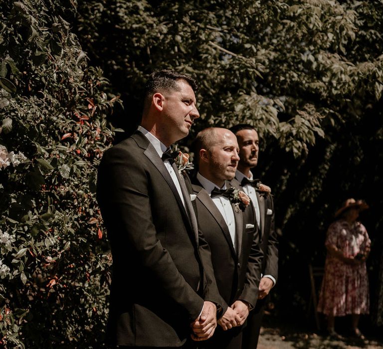 Groom and groomsmen stand together in black tie for the outdoor ceremony at Pennard House